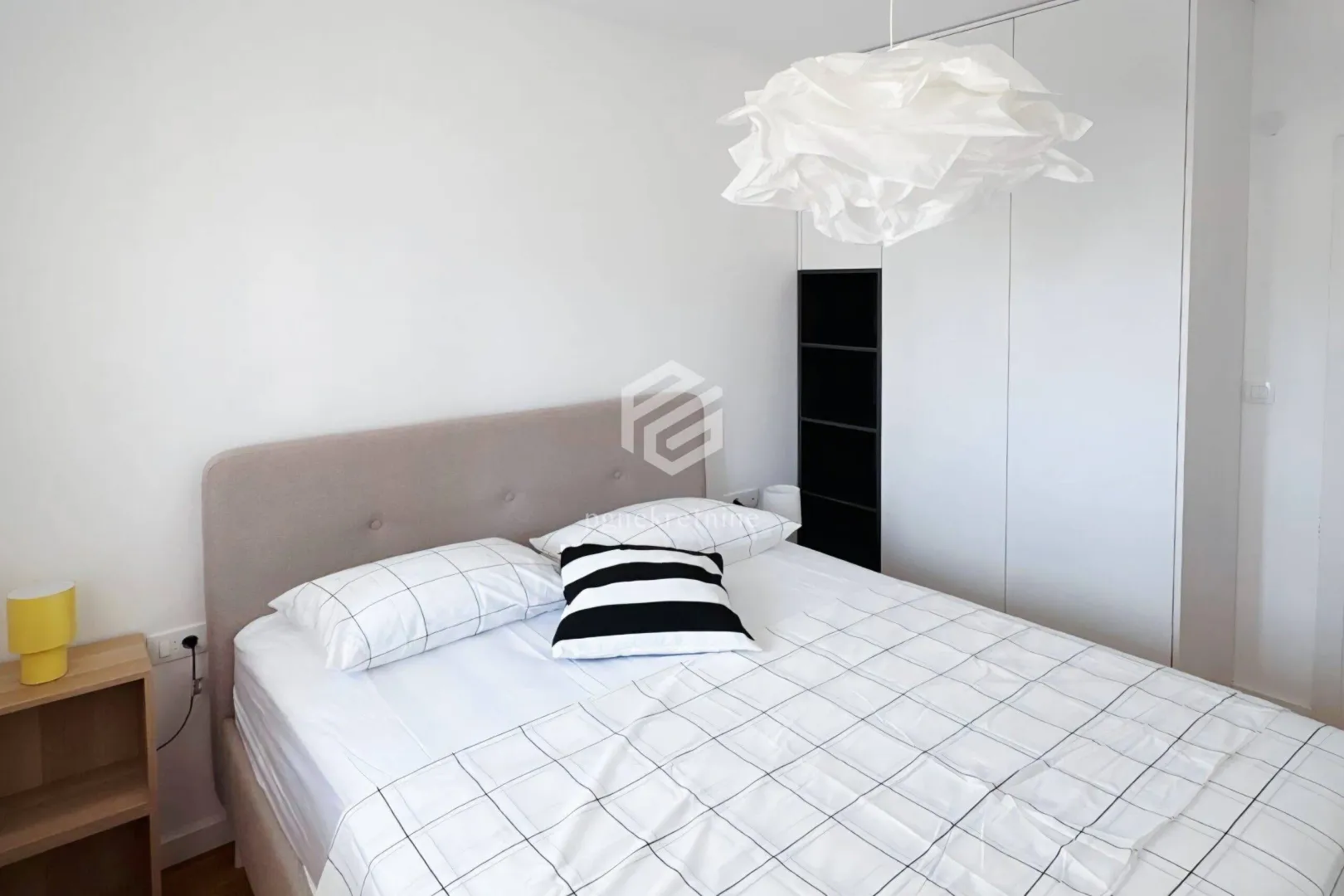 Bright bedroom with a double bed, white wardrobe, and a striking chandelier.