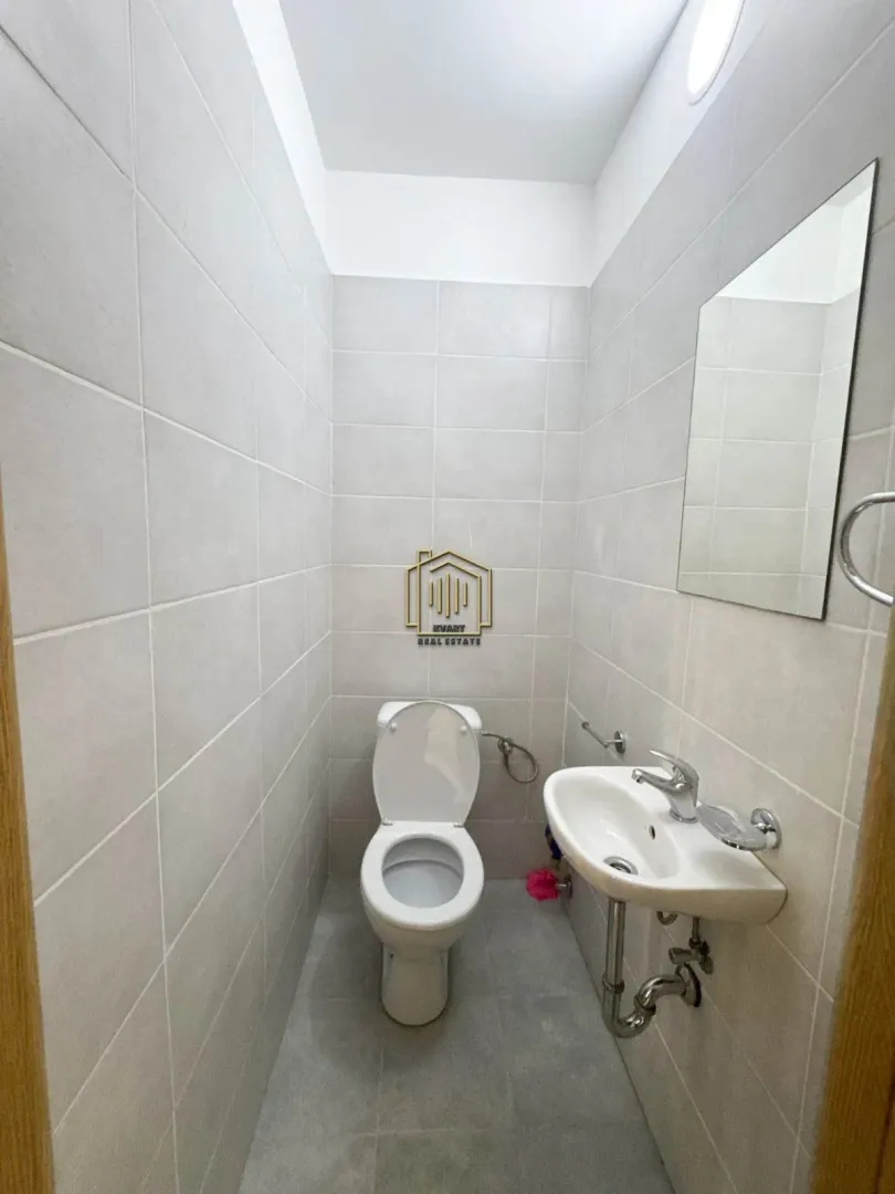Small bathroom with light-colored tiles, toilet, washbasin, and mirror.
