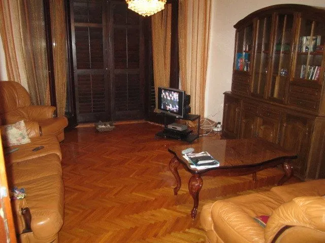 Dnevna soba sa kožnim namještajem, klupskim stolom i velikom drvenom vitrinom.