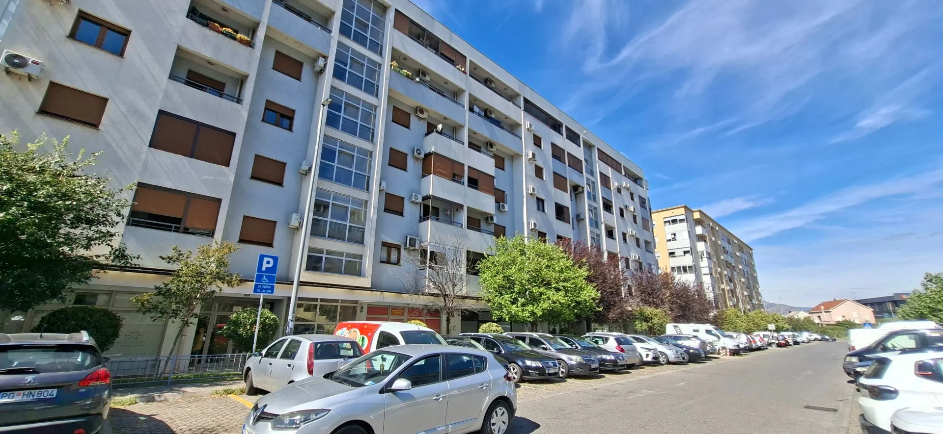 Exterior view of an apartment building with parking and greenery.