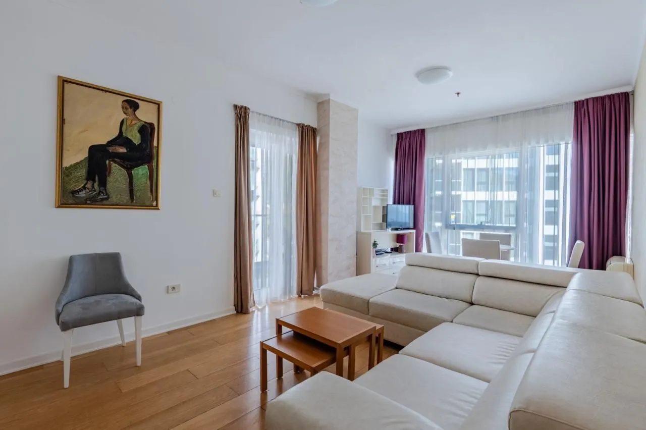 Bright living room with a sectional sofa, wooden coffee table, and large windows.