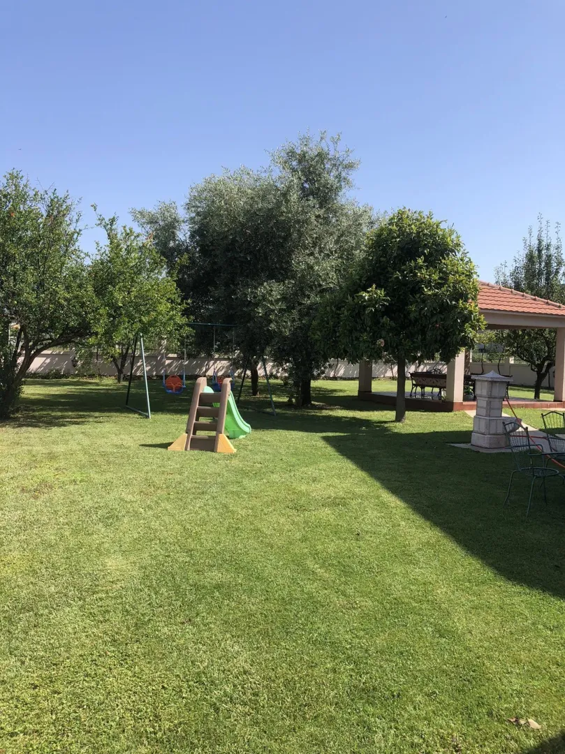 Spacious green yard with trees, a small children's slide, and a covered gazebo.
