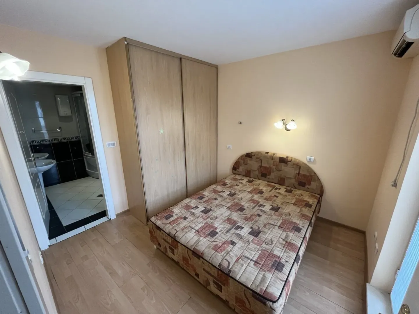 Jednostavna spavaća soba sa bračnim krevetom, velikim ormarom i otvorenim vratima prema kupatilu.