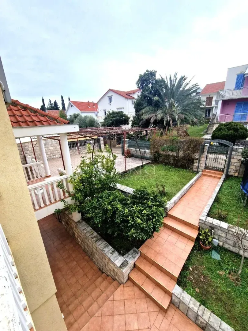 Pogled na uređeno dvorište i terasu kuće sa zelenilom.