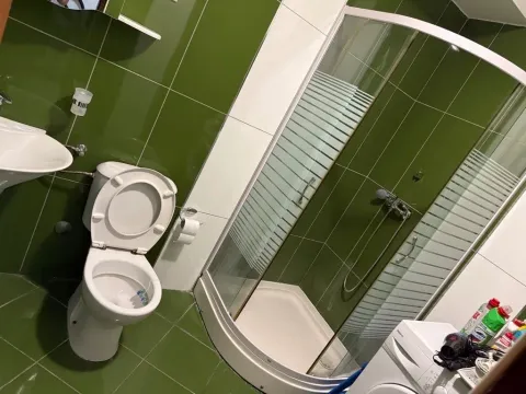 Bathroom with green tiles, shower cabin, toilet, and washing machine. - image 9