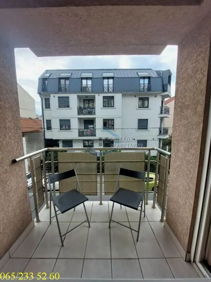 Manji popločani balkon sa dve stolice i pogledom na susednu zgradu.