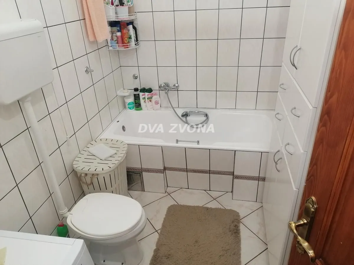 Smaller bathroom with a bathtub, toilet, and white cabinet.