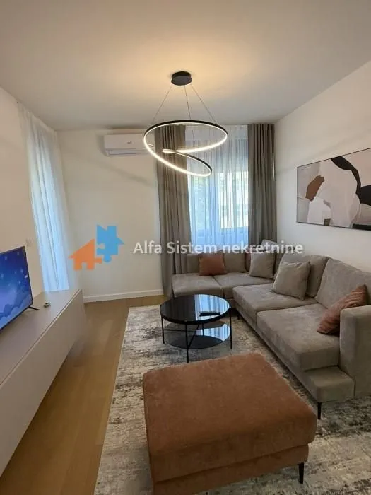 Udobna dnevna soba sa ugaonom garniturom, stočićem i modernim lusterom.