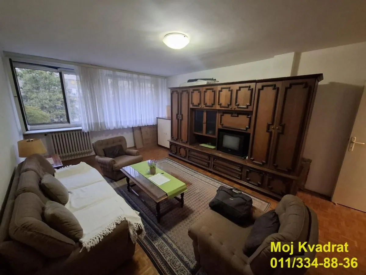 Dnevna soba sa garniturom za sedenje, velikim drvenim ormarom i prozorom.