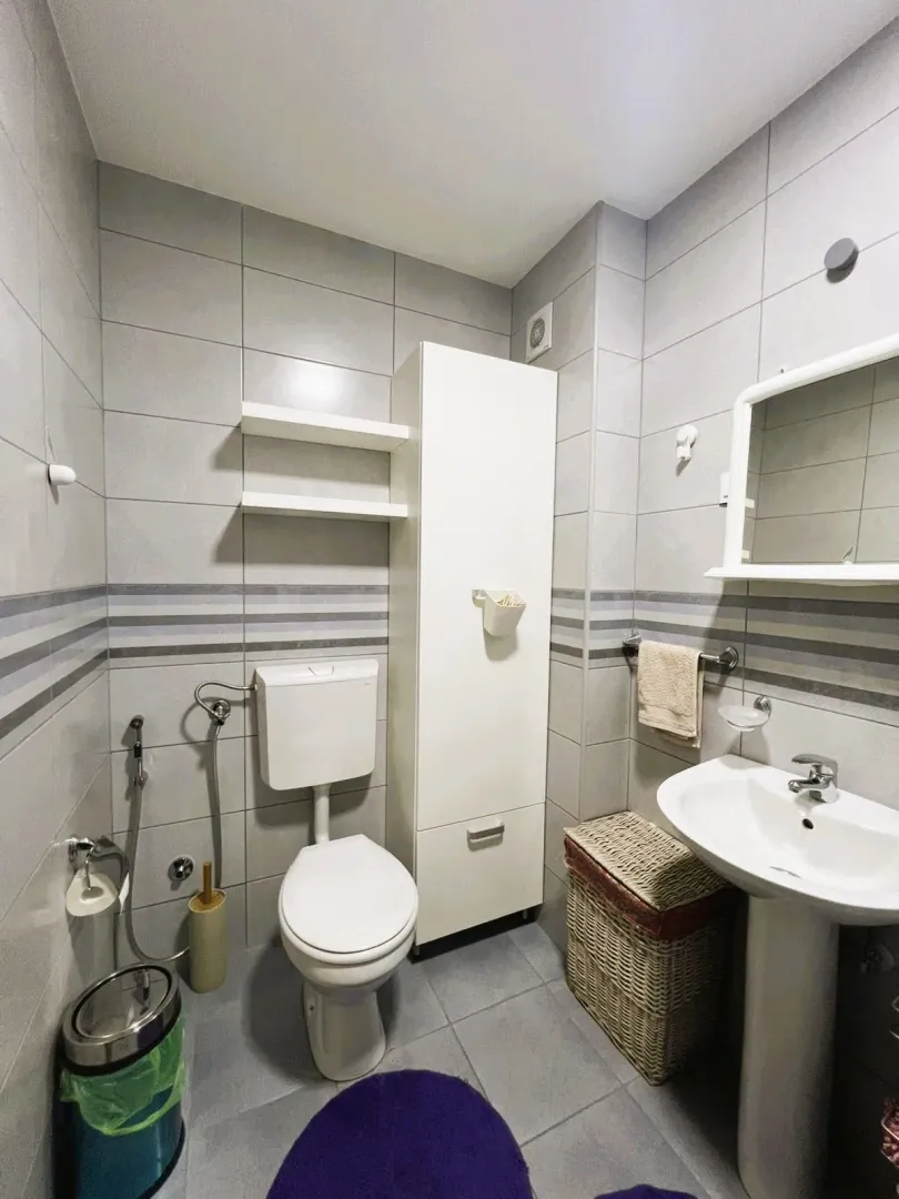 Manje kupatilo sa sanitarijama, umivaonikom, ogledalom i bijelim ormarićem.