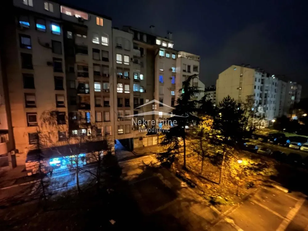 Pogled noću sa terase na okolne stambene zgrade i parking.