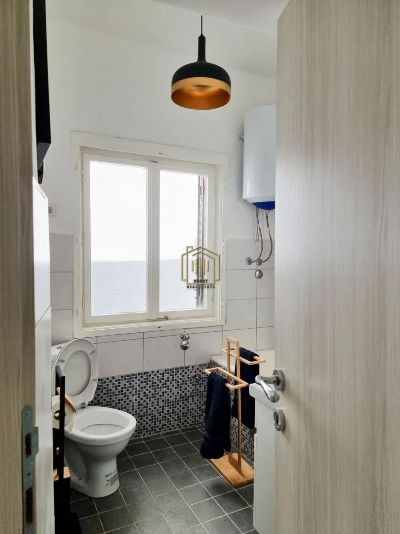 View of the bathroom with a toilet, window, and water heater.