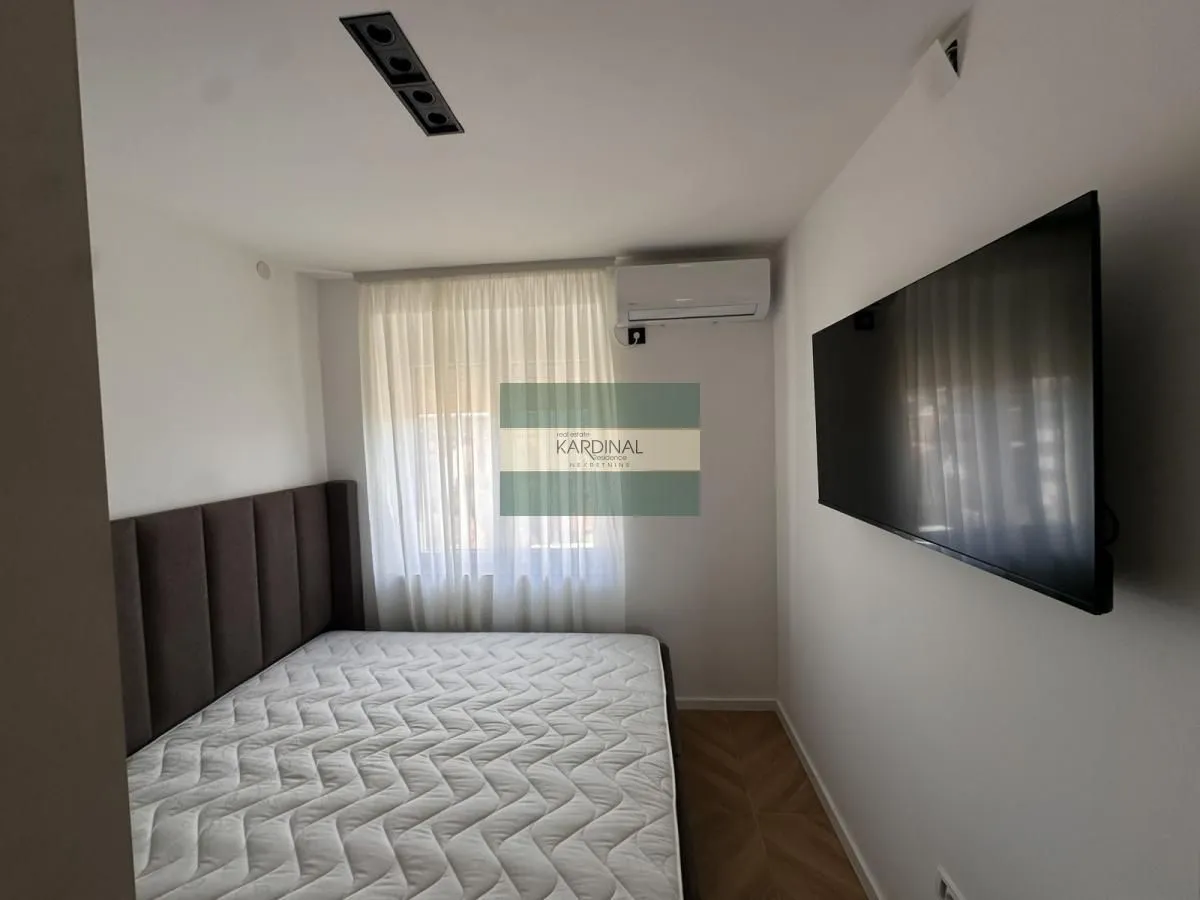 Nameštena spavaća soba sa bračnim krevetom, klima uređajem i zidnim televizorom.