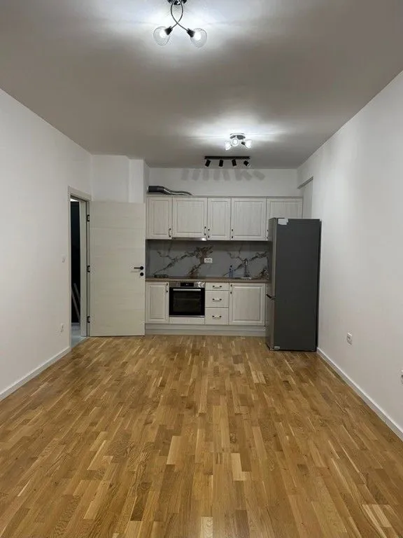 Manja kuhinja sa bijelim elementima i drvenim podom u praznoj prostoriji.