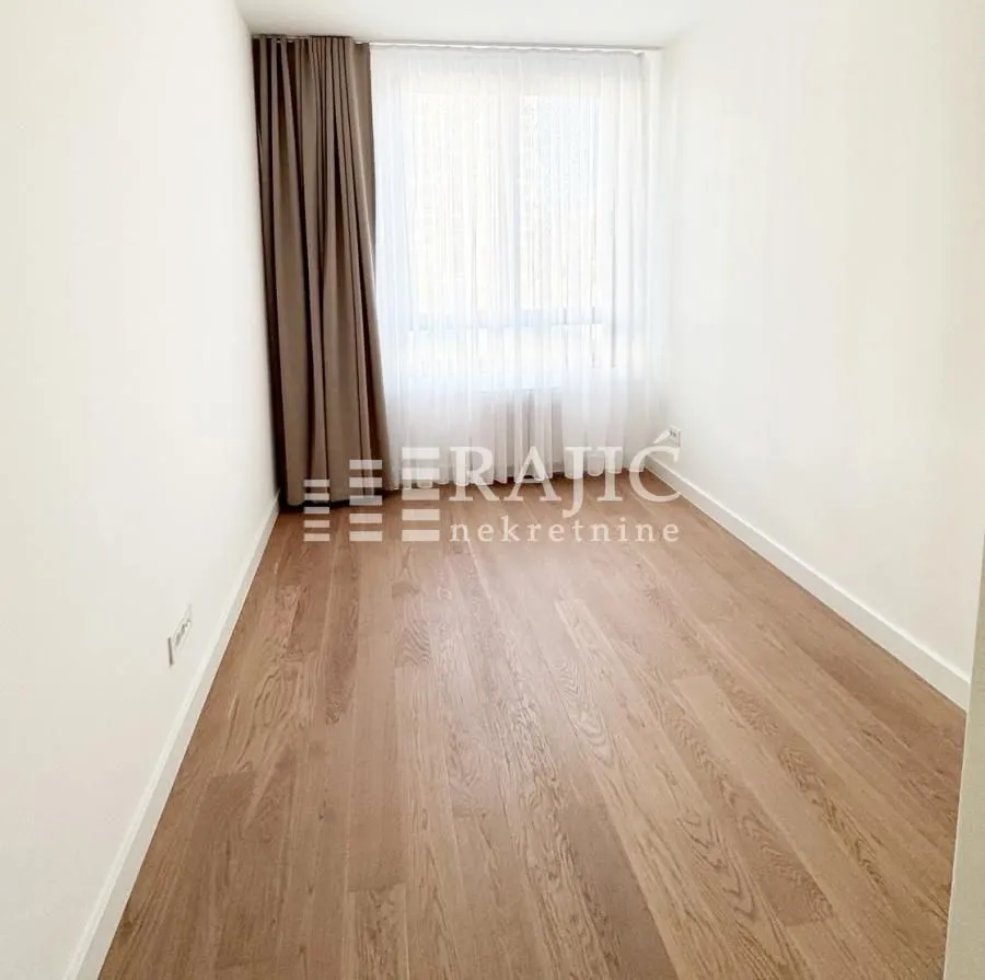Empty room with wooden flooring and a window with curtains.