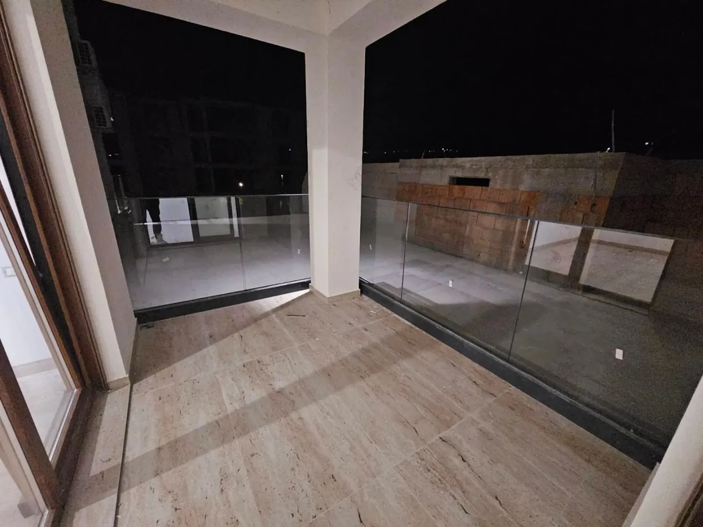 Prostrana pokrivena terasa sa staklenom ogradom i keramičkim podom.