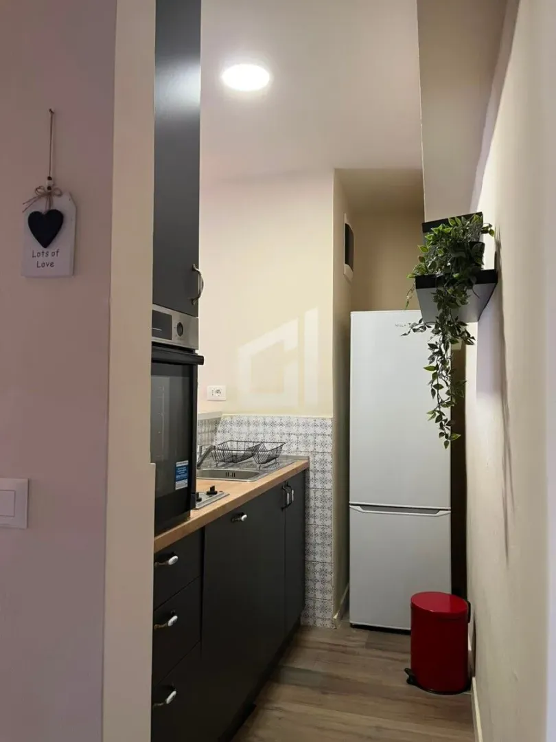 View of a narrow kitchen with dark cabinets and a white refrigerator.