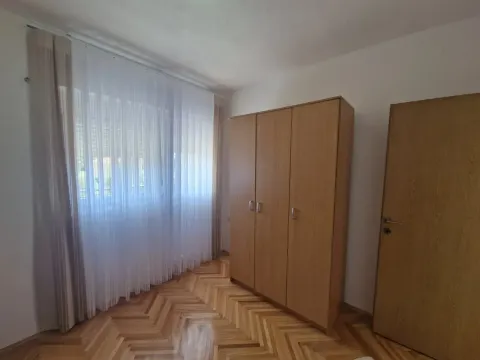 Bedroom with a wooden wardrobe, parquet flooring, and a large window with white curtains. - image 11