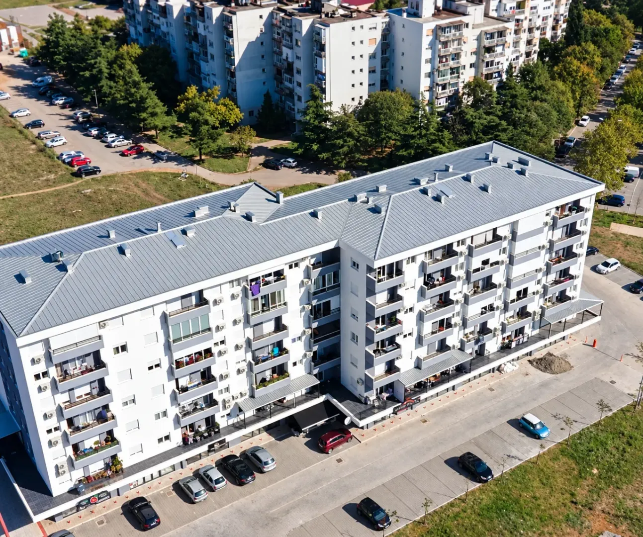 Pogled iz vazduha na stambenu zgradu sa okolnim parkingom i zelenilom.