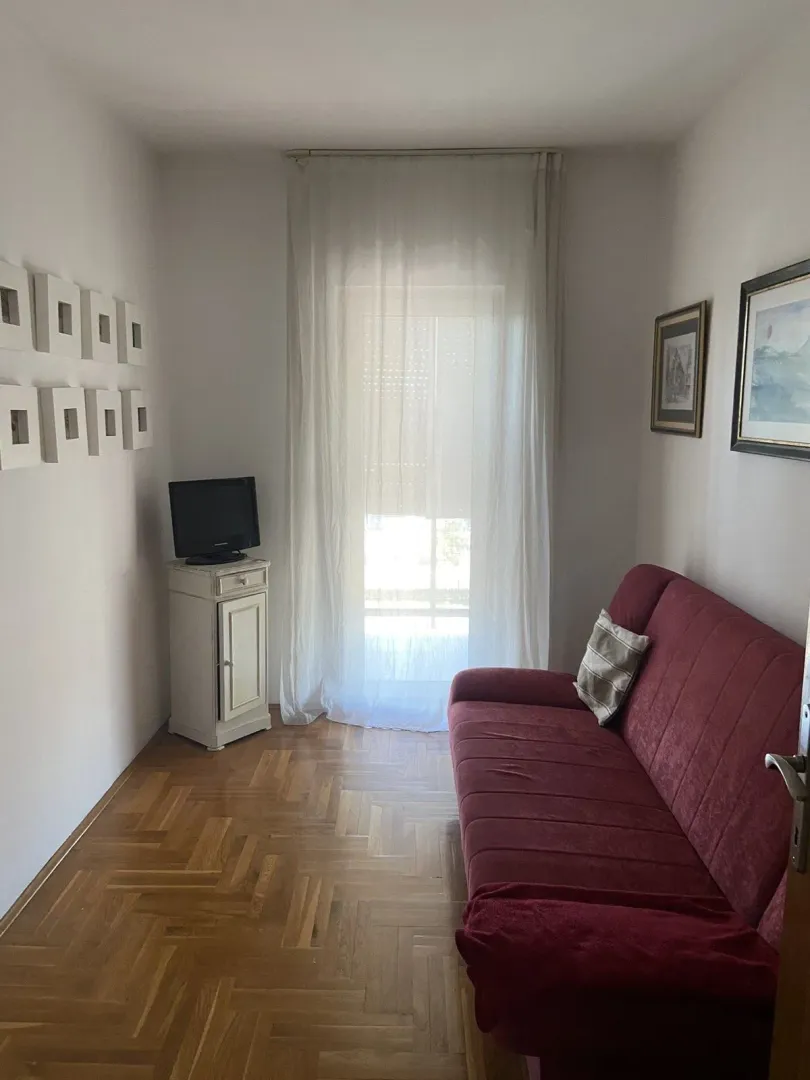 A small living room with a red sofa and parquet flooring.