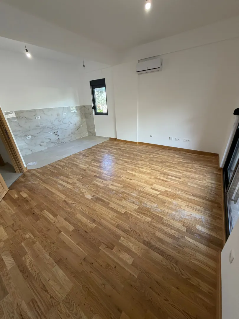 Prazna prostorija sa drvenim podom i pripremljenim dijelom za kuhinju.