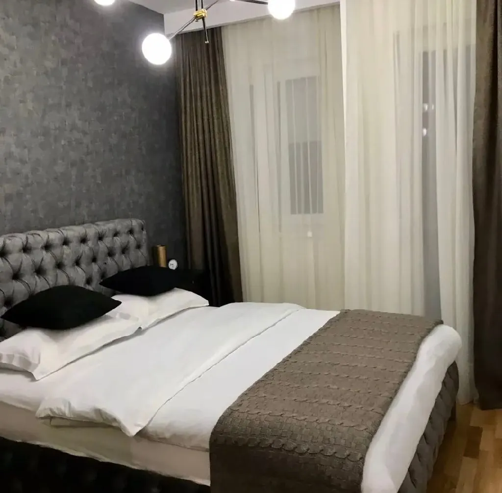 Moderna spavaća soba sa bračnim krevetom, sivim tapetama i zavjesama.
