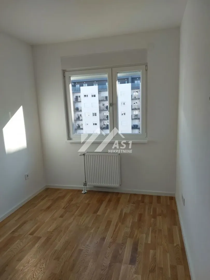 Prazna soba sa parketom i radijatorom ispod prozora.