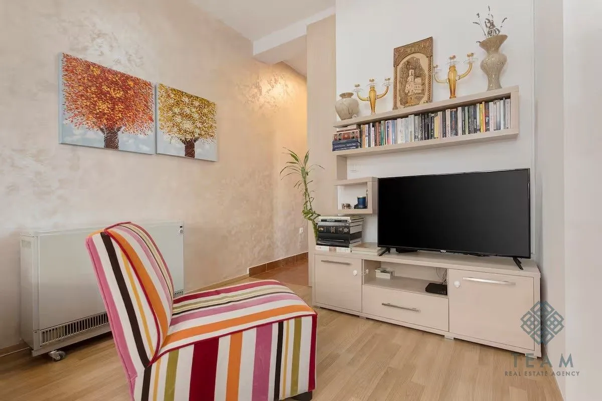 Living room with a colorful armchair, TV unit, and bookshelves.