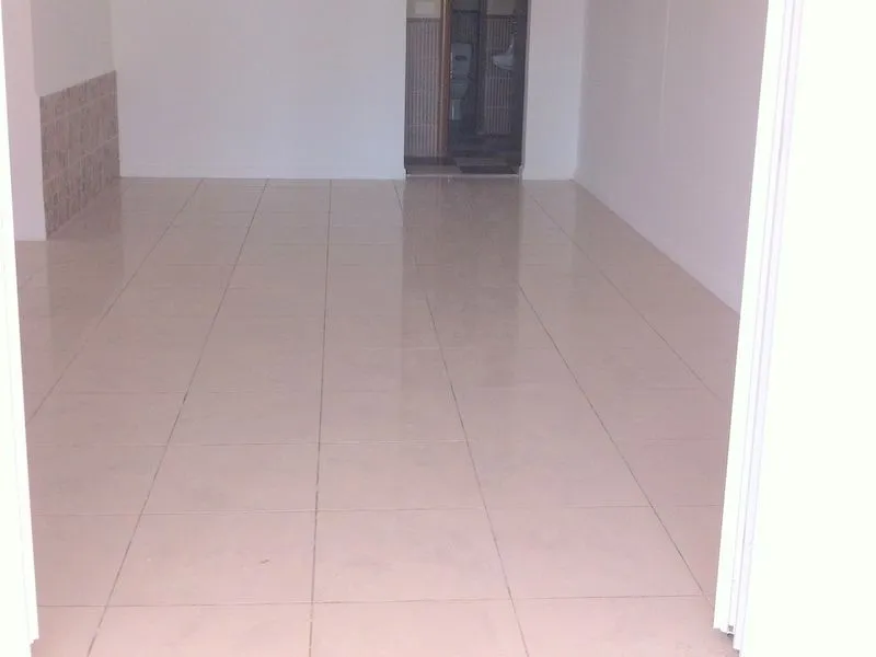 Prazna prostorija sa svijetlim pločicama i pogledom na kupatilo u pozadini.