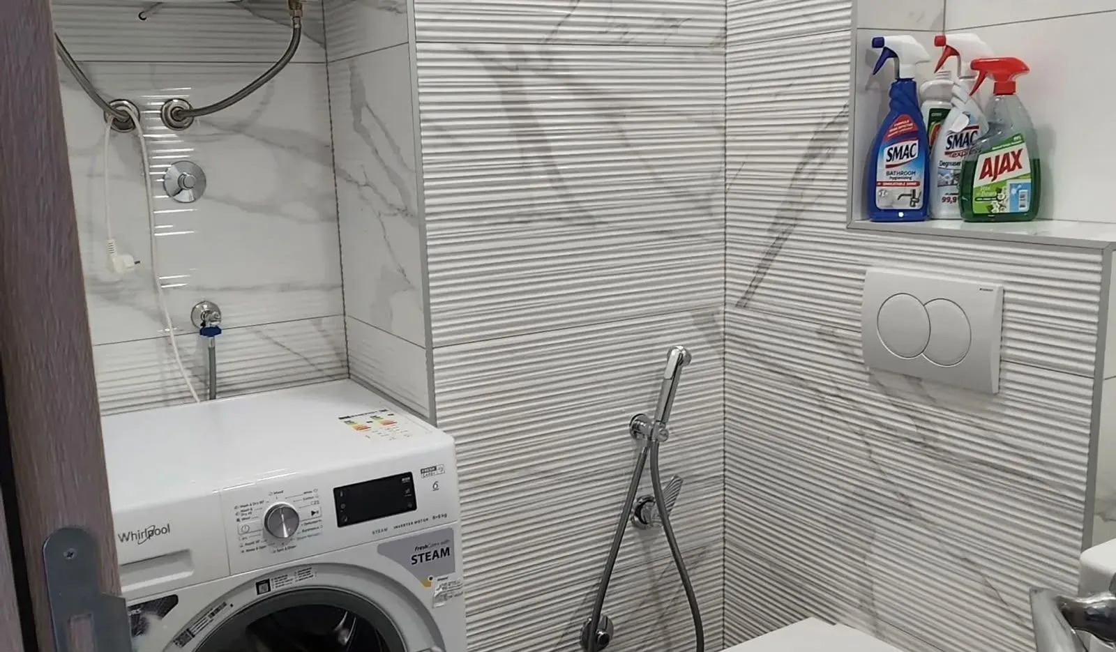 Small bathroom with a washing machine and cleaning products on a shelf.