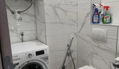 Small bathroom with a washing machine and cleaning products on a shelf. - image 13