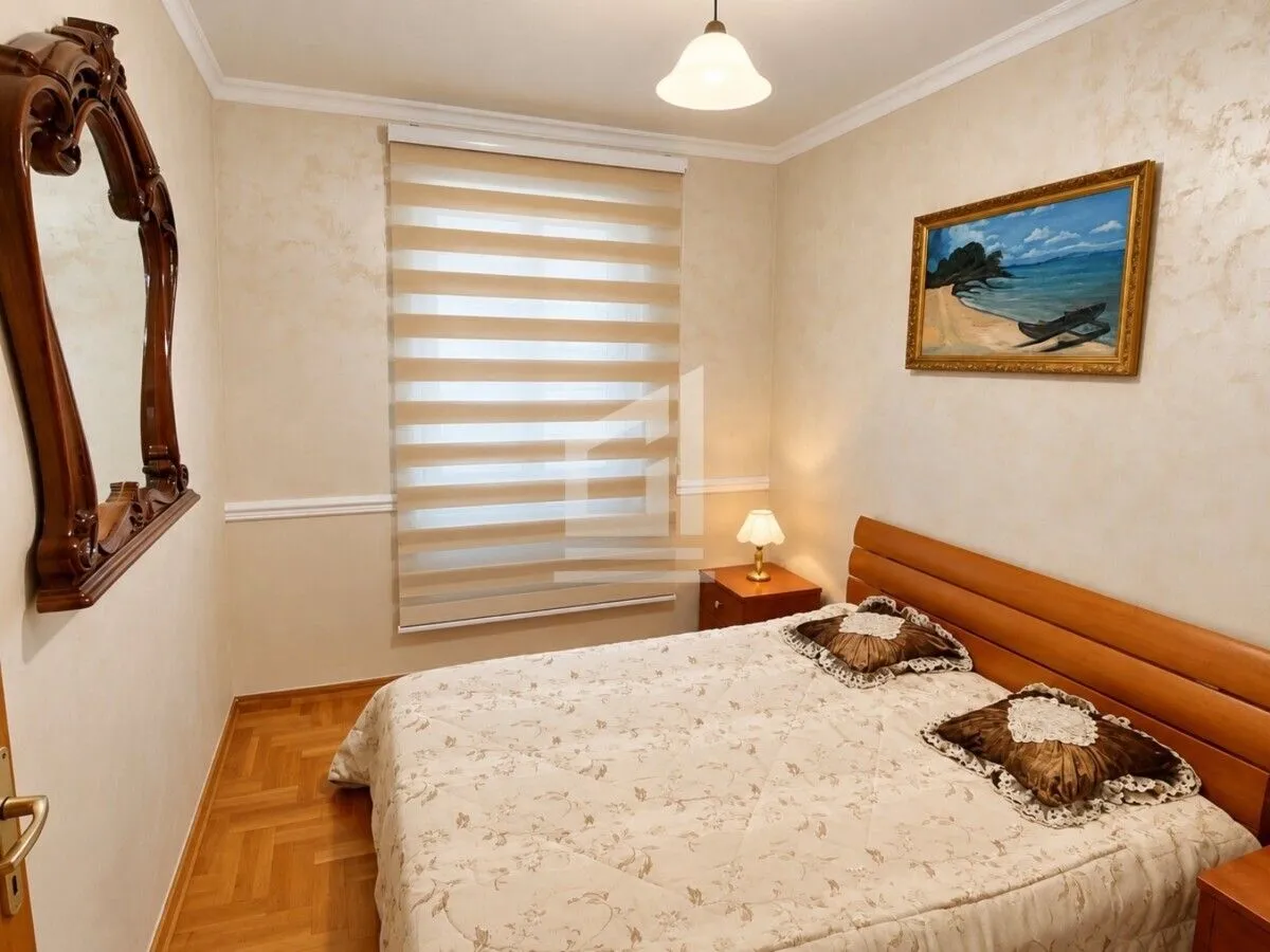 Furnished bedroom with a double bed, a window, and a wall mirror.