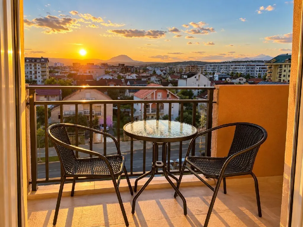 Namješten balkon sa stolom i dvije stolice i pogledom na grad pri zalasku sunca.