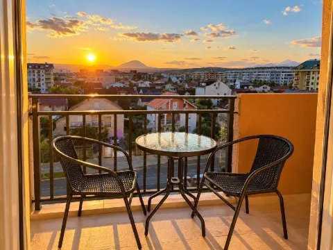 Namješten balkon sa stolom i dvije stolice i pogledom na grad pri zalasku sunca. - image 6