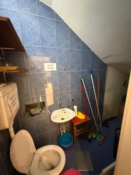 A small bathroom with blue tiles, a sink, and a toilet. - image 9