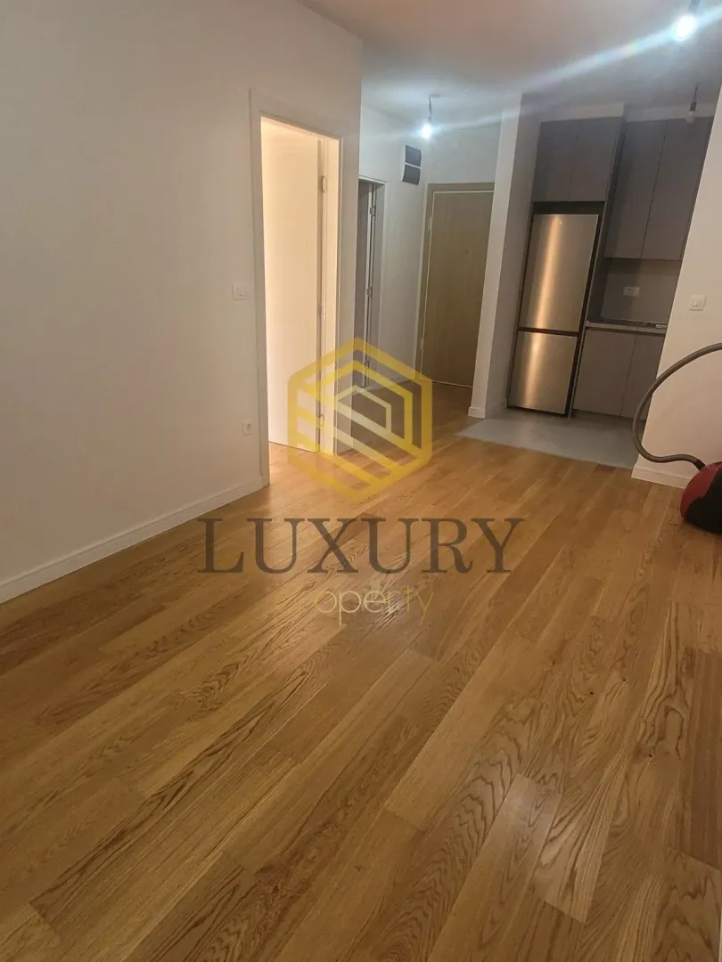 Living room with hardwood flooring and a view of the kitchen in the background.