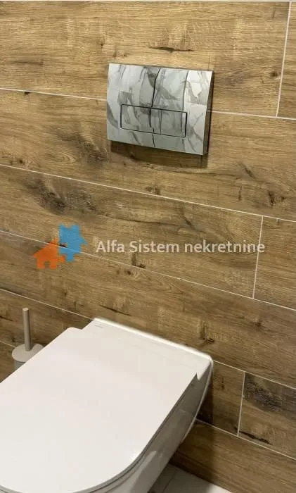 Kupatilo sa zidnim pločicama u imitaciji drveta i ugradnom šoljom.
