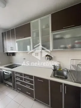 Pogled na kuhinju sa tamnim elementima, sudoperom i ugrađenom rernom. - image 9