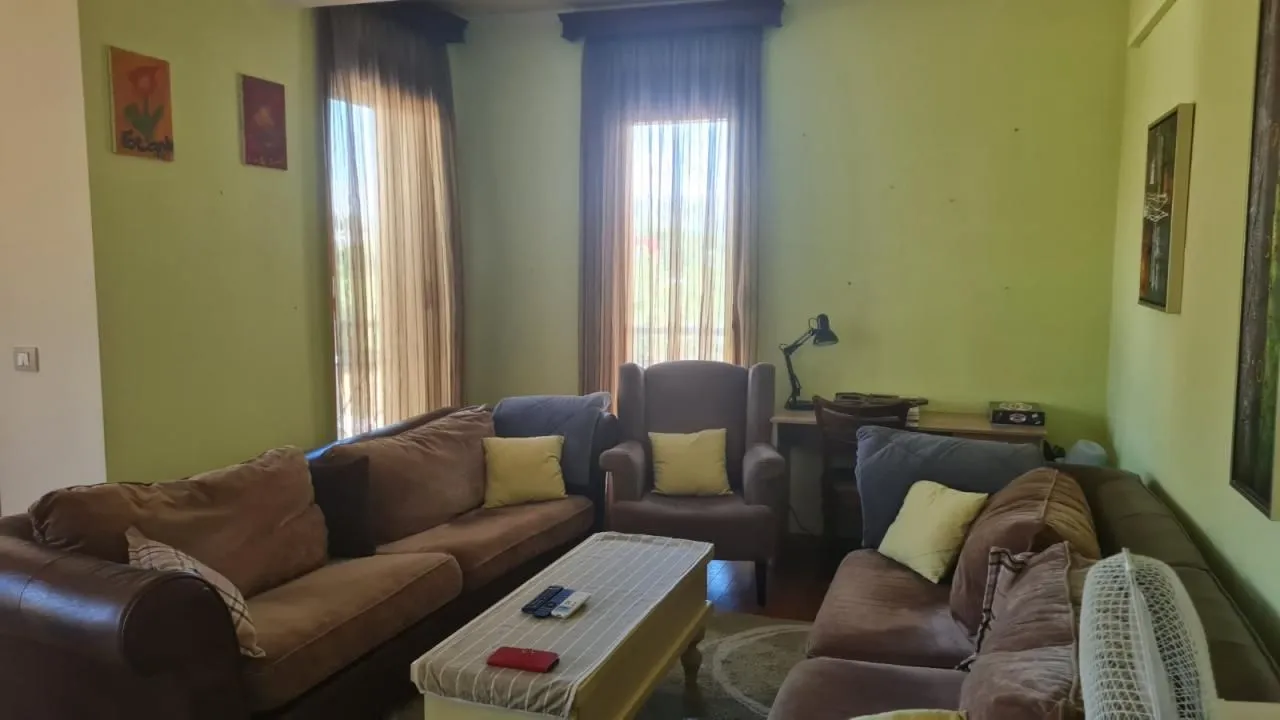 Dnevna soba sa garniturom za sjedenje, stočićem i prozorima sa zavjesama.