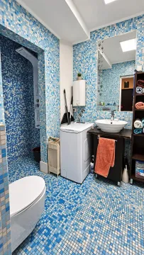 Bathroom lined with blue mosaic tiles featuring a shower cabin, washbasin, and washing machine. - image 14