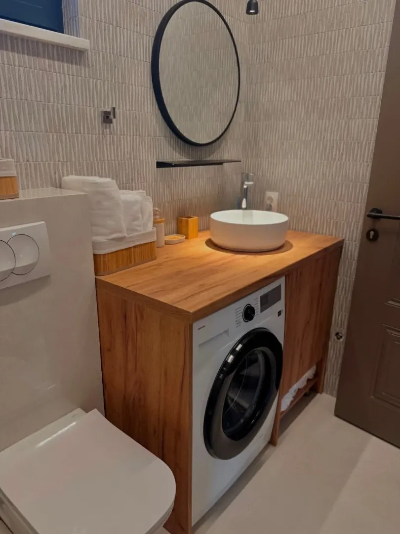 Modern bathroom with a wooden vanity, basin, and washing machine.