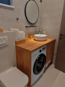 Modern bathroom with a wooden vanity, basin, and washing machine. - image 4