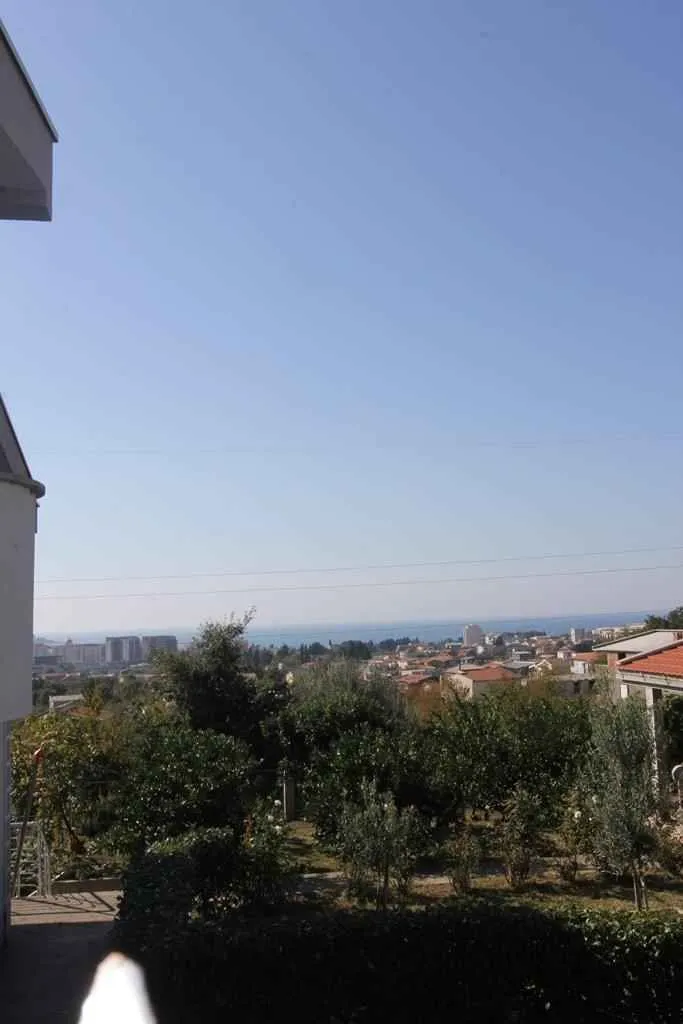Pogled sa visine na okolno zelenilo, naselje i more u daljini.