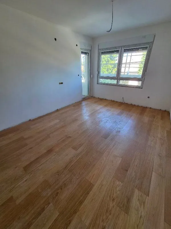 Empty unfinished room with installed parquet flooring and windows.