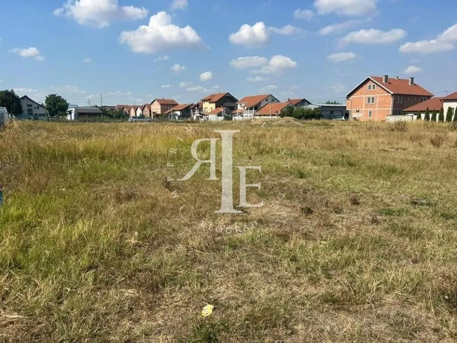 Pogled na ravno građevinsko zemljište sa travom u mirnom naselju sa porodičnim kućama.