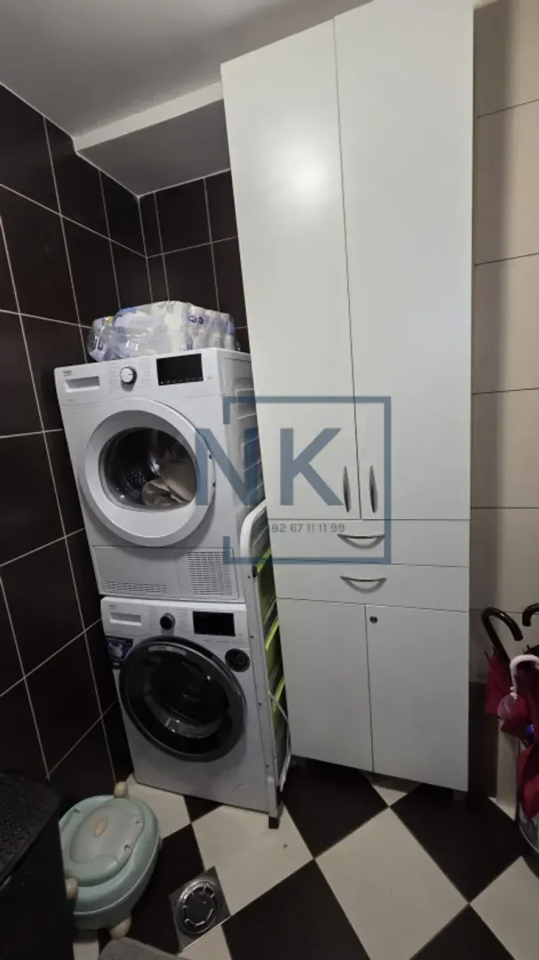 Kupatilo sa mašinom za pranje i sušenje veša i bijelim ormarićem.