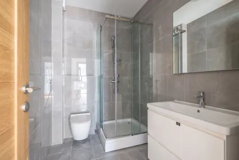 Moderne kupatilo sa tuš kabinom, umivaonikom i wc šoljom obloženo sivim pločicama. - image 3