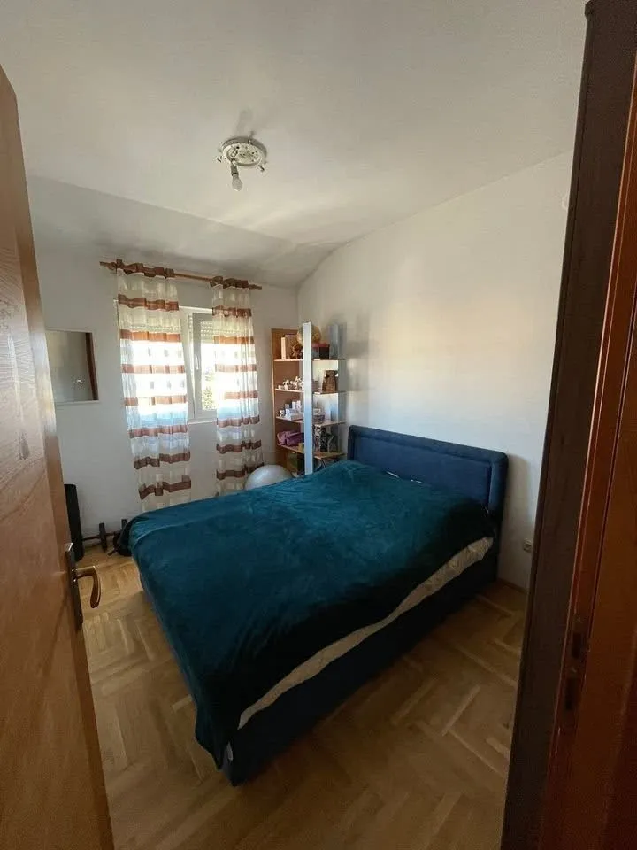 Spavaća soba sa bračnim krevetom, parketom i prozorom.