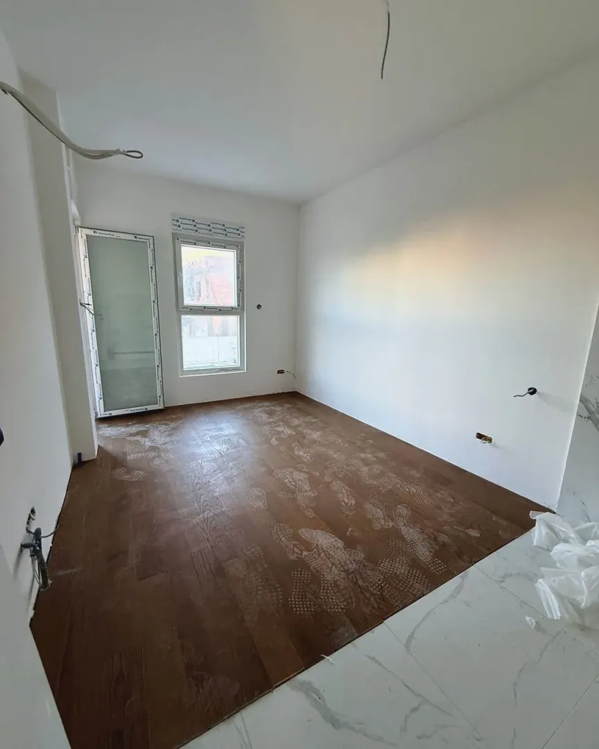 Empty room under construction with wooden flooring and white walls.