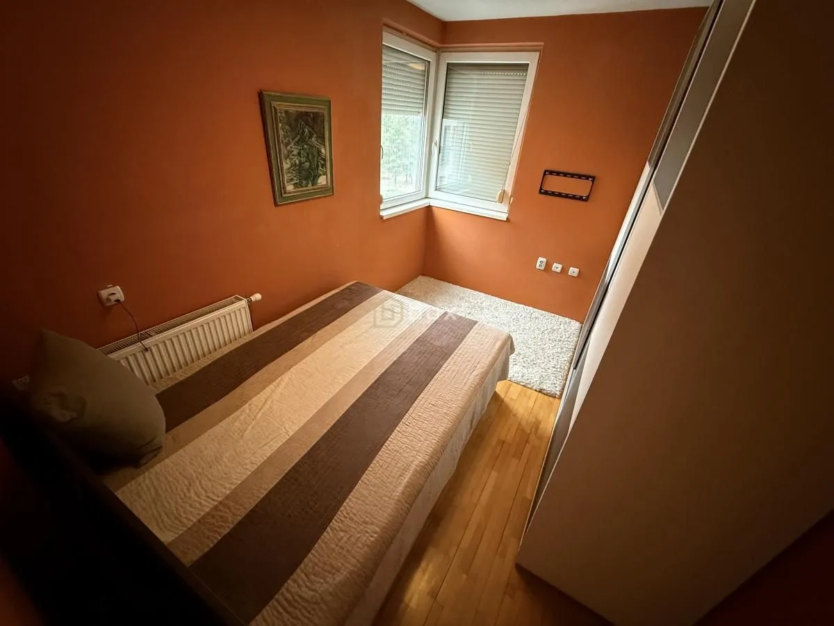 Manja spavaća soba sa bračnim krevetom, ormarom i narandžastim zidovima.